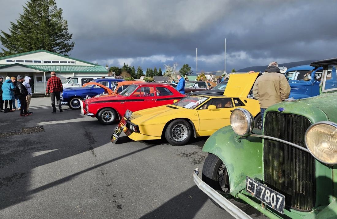 Vintage and classic cars on display at the school grounds, with a yellow Heron sports car and a green pre-war truck in the foreground
